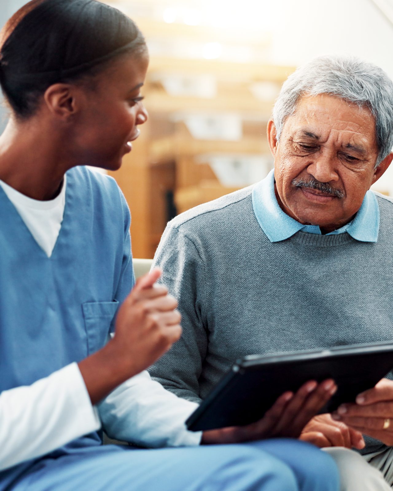 A nurse reviewing information on a tablet with an older adult on a sofa