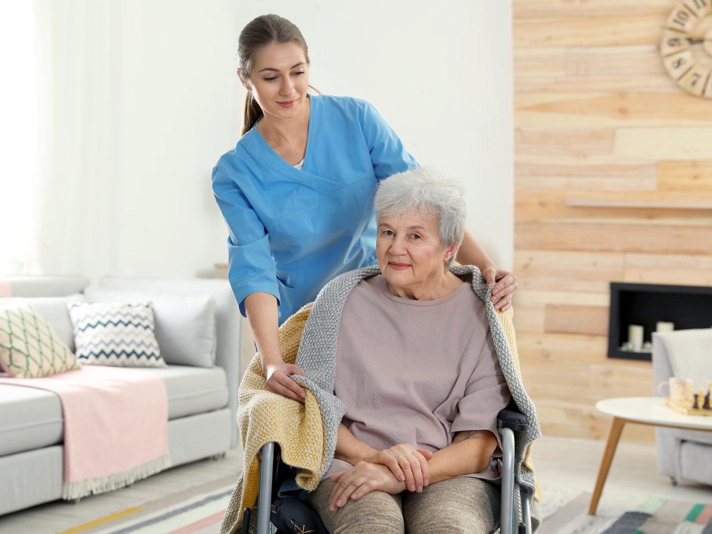 A caregiver sitting with an older adult wrapped in a blanket at home