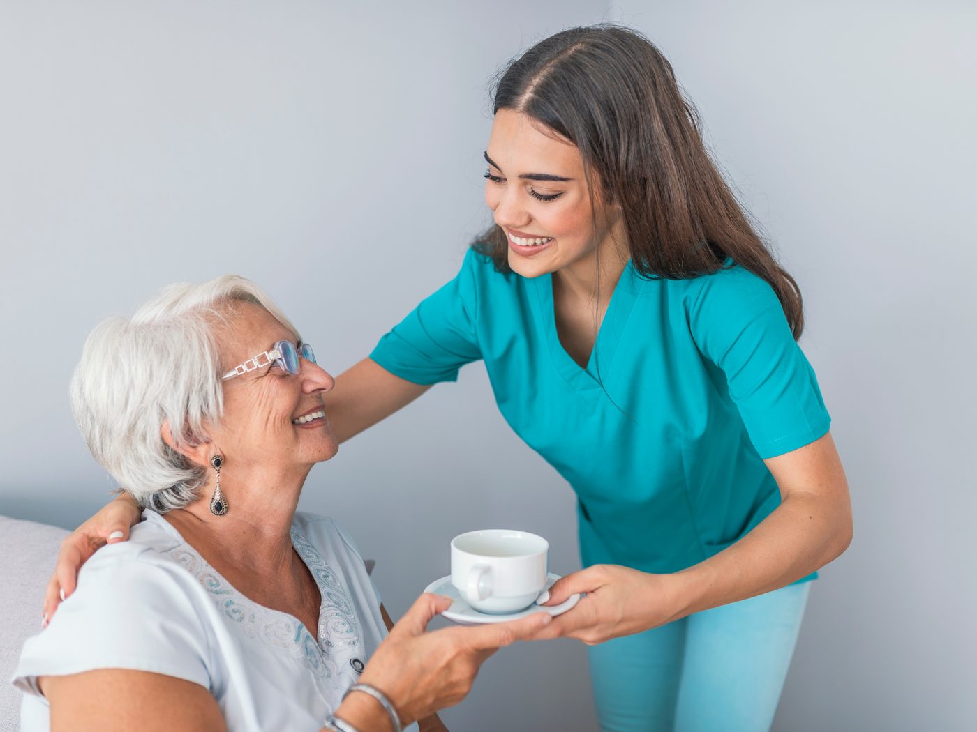 A caregiver serving a warm drink to an older adult in a bright living room