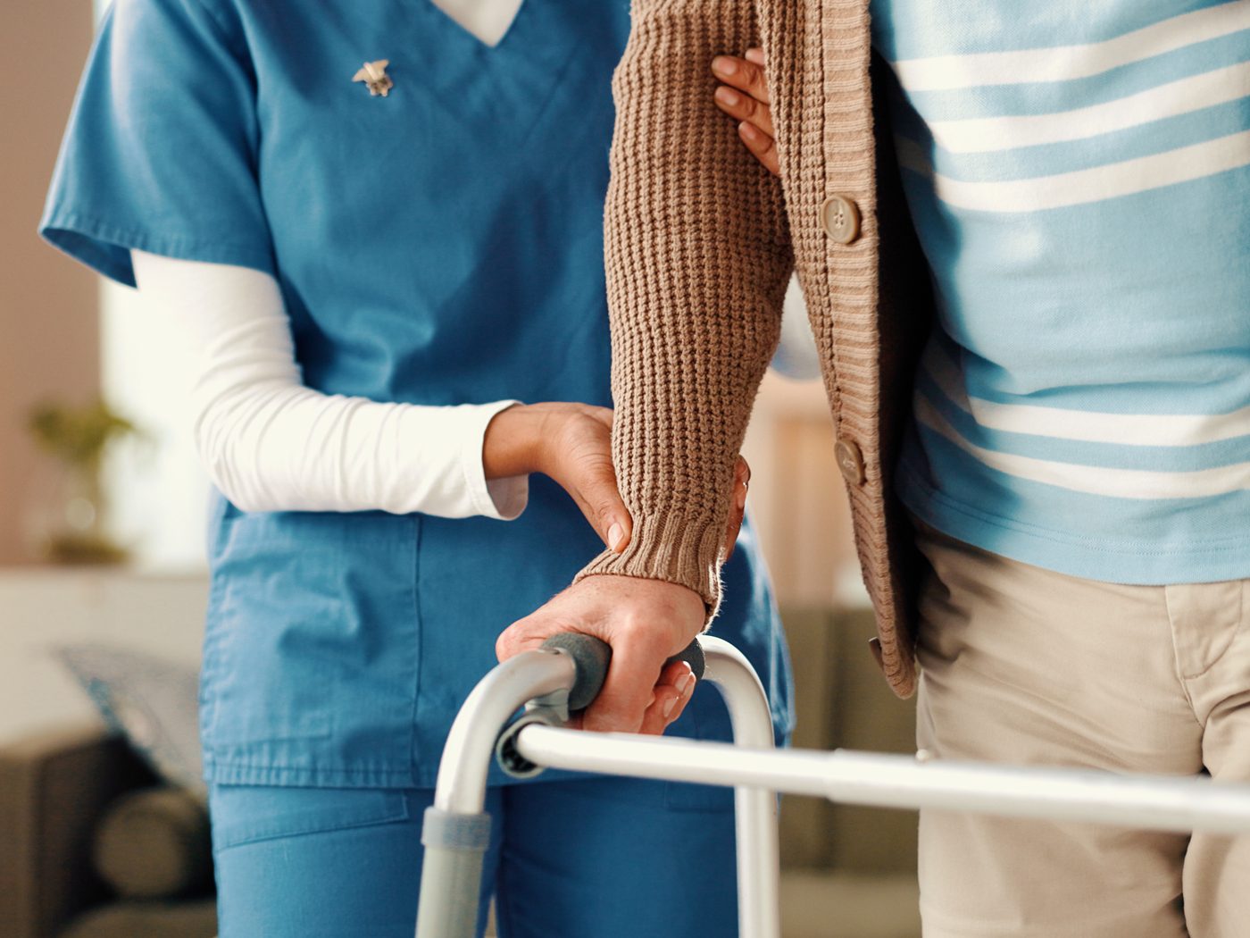 A caregiver steadying an older adult who is using a walker at home